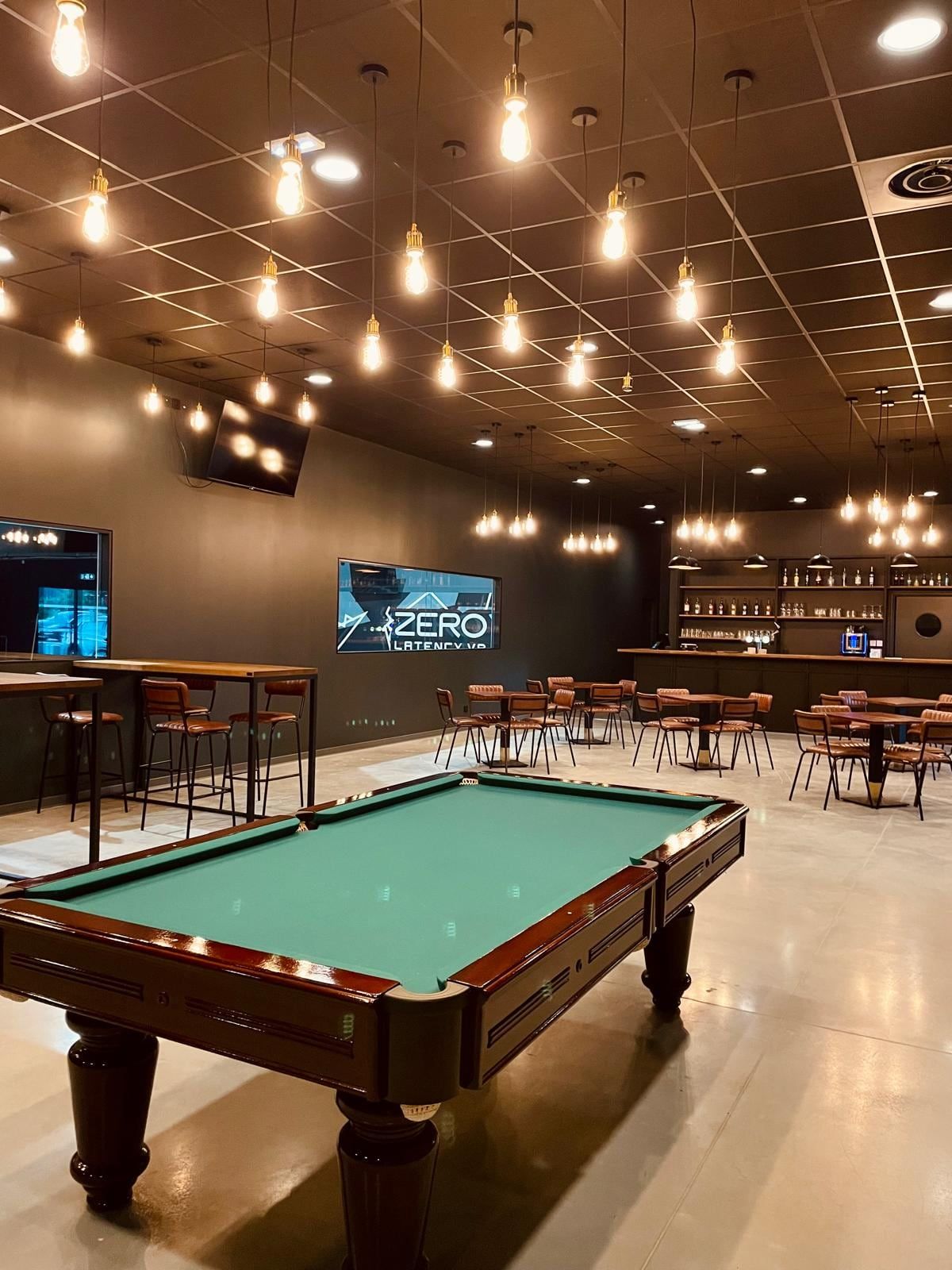 La salle du bar à jeux du Bastion : tables, canapé, billard et cibles de fléchettes